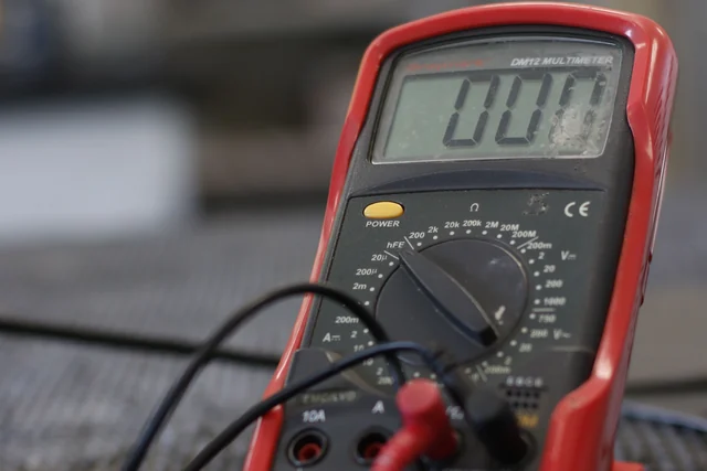 A red digital multimeter with test leads resting on a workbench