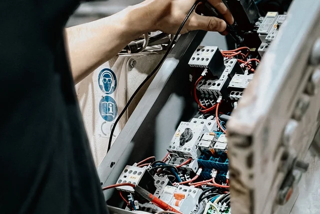 Two hands using side cutters on wiring inside an open electrical control panel